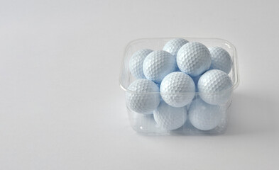 White golf balls, collected and cleaned, placed in a clear plastic basket, ready to use. White background.