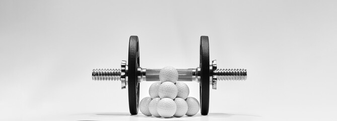 Golf balls with dumbbell and iron weights on white background. Training concept for more strength.