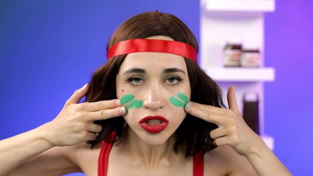 An angry girl fighter paints her face with makeup and puts a red ribbon on her head.