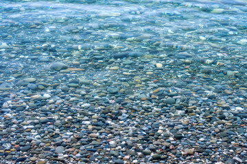 Multicolored sea pebbles in calm clear water, perspective view.