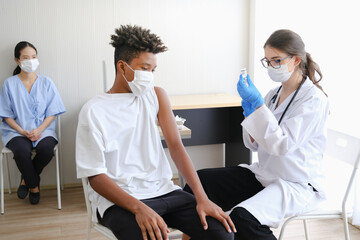 Obraz premium Caucasian doctor woman or nurse giving flu or antiviral vaccine to African American man in hospital or clinic