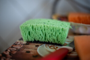 green porous sponge for washing dishes on the table. out of focus. blurred kitchen background.