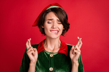 Photo of worried helper lady close eyes crossed fingers bite lip wear elf costume hat isolated red...