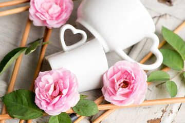 Damask rose flowers, white coffee cup on an old wood background.