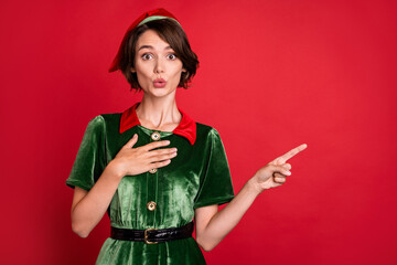 Photo of young amazed shocked lady santa helper point finger empty space news isolated on red color...