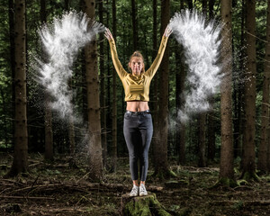 Sportswoman throwing white flour while standing on tree stump in forest