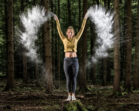 Sportswoman throwing white flour while standing on tree stump in forest