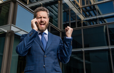 angry entrepreneur in suit shouting while phone conversation outside the office, frustration.