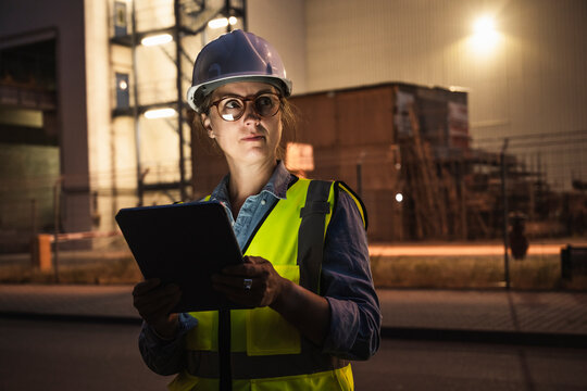 Thoughtful female engineer with digital tablet standing in front of industry