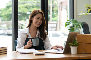 Young asian woman startup small business freelance sitting with parcel box and computer laptop on wood table in living room at home, Online marketing packing box delivery concept