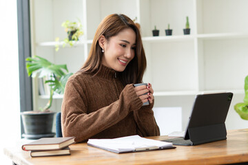 Beautiful smiling Asian female blogger dressed casual sitting and using laptop computer on the wood table in the cafe and restaurant