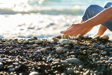 The hand of a man folding pebbles into a pyramid on the seashore.