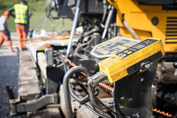 Control panel of the asphalt paver close-up and two worker in the background controling the paving process.