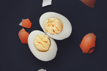 The halves of a peeled boiled egg lie on a dark background next to a brown broken shell. Healthy food.