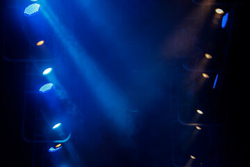 Stage spotlights shine in the dark through the smoke.