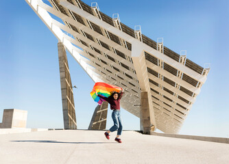 Woman holding rainbow flag near solar energy panel