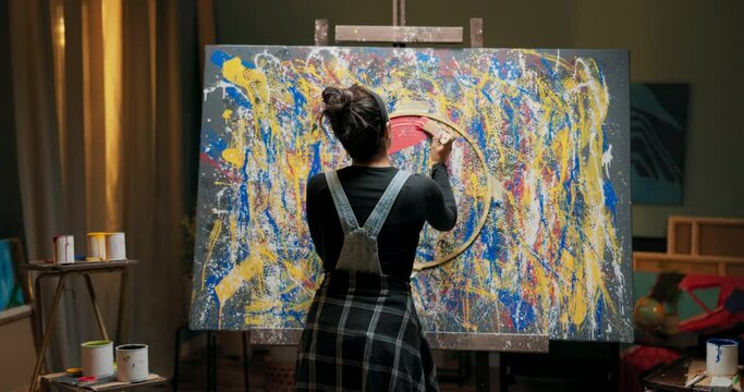 A young novice artist creates a new painting for auction, bidding, exhibition, in hand she holds a can of red paint and a brush with which she applies the color on the rim of a glued circle