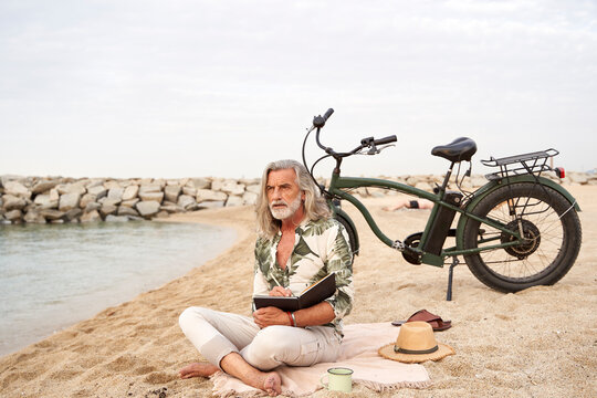 Man writing in book while sitting by bicycle at beach