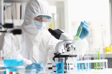 Woman chemist in protective suit conducts laboratory research on green liquid