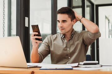 Naklejka premium Young business man working at home with laptop and uses a smartphone