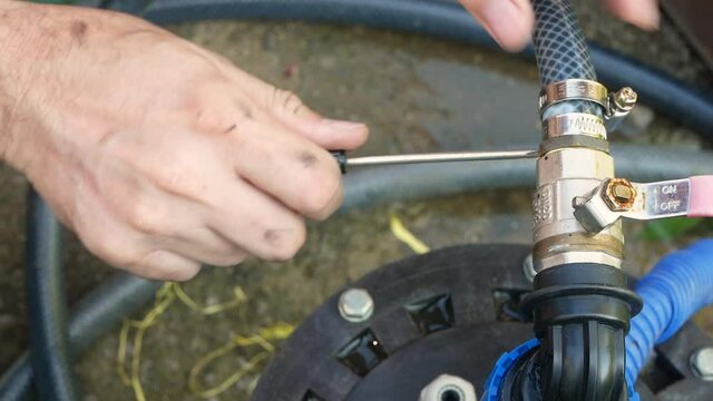 Installation of a submersible pump for water supply in the country. Close-up of a plumber's hands installing a hose clamp on the water hoses to fix leaks. Outdoor plumbing repair