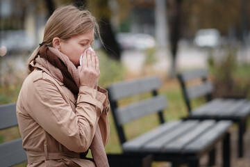 Adult woman blowing nose with handkerchief in park.