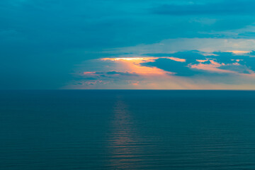 Naklejka na ściany i meble Sunset on the sea on a cloudy rainy day, sunlight on the dark surface of the sea