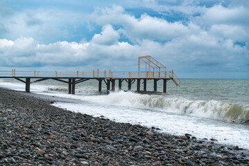 The pier cuts the sea waves off the coast during a storm under a cloudy sky during rain