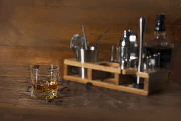Glass of whiskey on vintage wooden counter in the background with bar tools