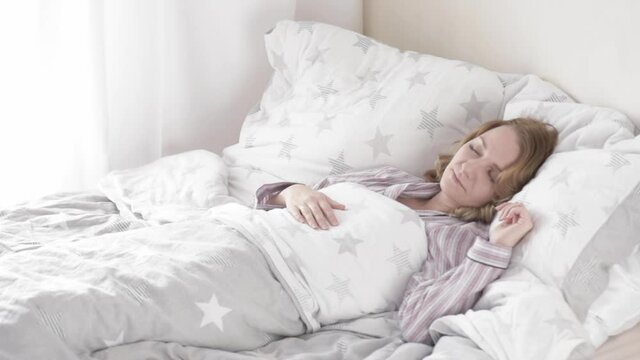 Beautiful young Woman is Sleeping on white Pillow. Girl in Pajamas is Waking up. Caucasian Female on Bed early in Morning.