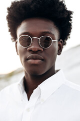 Portrait of a stylish African man in sunglasses, and a white shirt, fashion posing