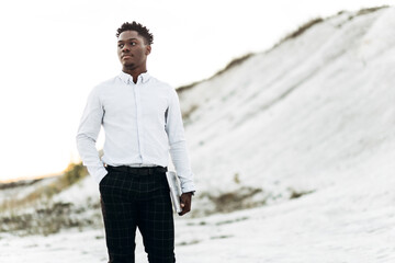 Elegant black man holding his laptop, against the background of white chalk rocks and mountains