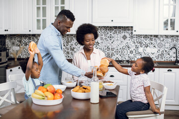 African american wife and husband preparing tasty breakfast for their two cute daughters. Positive and beautiful family spending morning time together at home. Healthy nutrition.