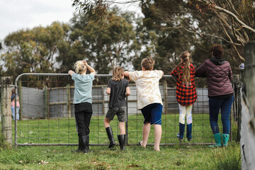 Fototapeta premium Woman with four children resting on farm gate looking into the field