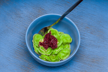 on the wooden surface painted with bright paint there is a bowl with turkey and spinach dumplings seasoned with hot sauce and a fork