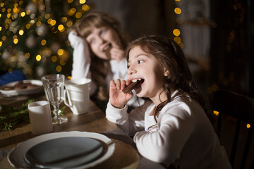 Two Kids sisters eat Christmas cookies  in the kitchen at home. 
