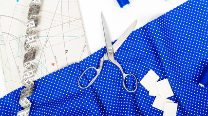 Tailoring. Fashion designer workspace top view. Sewing equipment, tape measure, blue fabric, pattern and scissors on cloth.