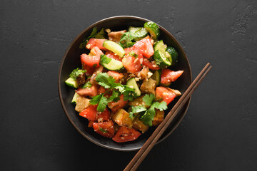 Chinese crispy spicy eggplant with cucumber, garlic, tomatoes, fresh cilantro leaves in oyster sauce and black vinegar on black background. View from above.