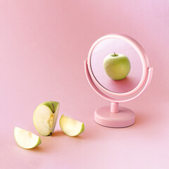 Mirror reflection of a fresh green apple and sliced fruit against pastel pink background. Minimal concept