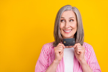 Photo of aged woman happy positive smile curious look empty space credit card money isolated over yellow color background