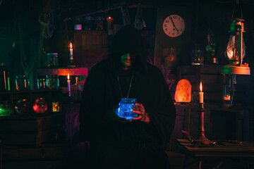 Fototapeta na wymiar alchemist magician holds a flask with a potion in hands. Sorcerer is witcher in dark laboratory