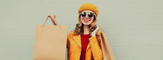 Autumn portrait of beautiful happy smiling young woman with shopping bags wearing an yellow jacket, beret on gray background