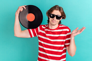 Portrait of attractive confused clueless guy using vinyl disk isolated over bright teal turquoise...