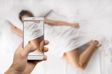man hand making photo or video using mobile phone while girl lying on bed at home
