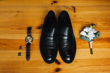 Wedding accessories on a wooden parquet background: black shoes, boutonniere, cufflinks.