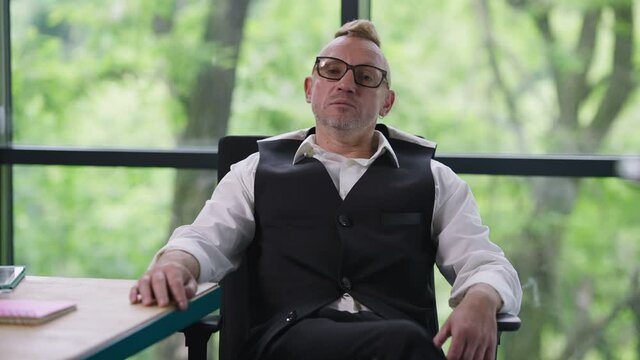 Portrait of confident business owner conferencing online talking in video chat. Front view of serious Caucasian man in eyeglasses with tattoo and mohawk haircut brainstorming. Web camera point of view