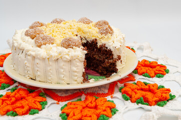 Delicious homemade stuffed chocolate cake decorated with grated white chocolate and dulce de leche coconut fudge truffles. Crochet tablecloth background.