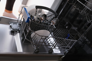 White plates and cutlery in open dishwasher closeup