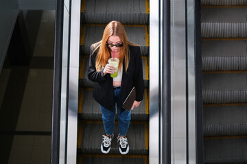 beautiful young woman walking the escalator of a shopping mall with coffee in her hands