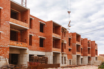 Construction Site. Сrane lifts the beam, Pile of sand and shovel at the construction site. cobstruction site background with built and unfinished houses